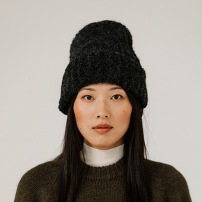 Woman wearing a charcoal grey rib knit beanie against a plain background