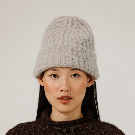 Person wearing a light gray knit beanie against a plain background