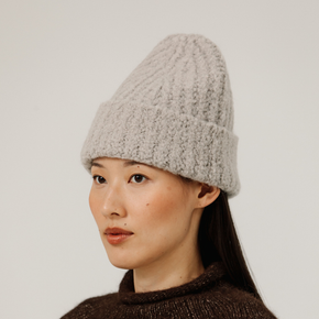 Woman wearing a light gray rib knit beanie against a plain background