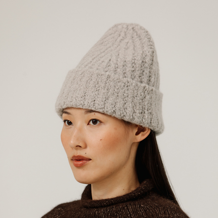 Woman wearing a light gray rib knit beanie against a plain background
