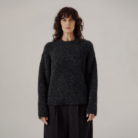 Woman wearing a dark gray boucle sweater against a plain background