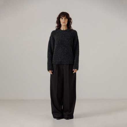 Person wearing a dark gray boucle sweater and black pants on a plain background