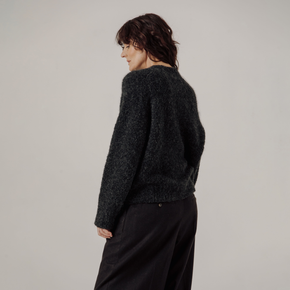 Person wearing a dark gray boucle sweater and black pants on a plain background