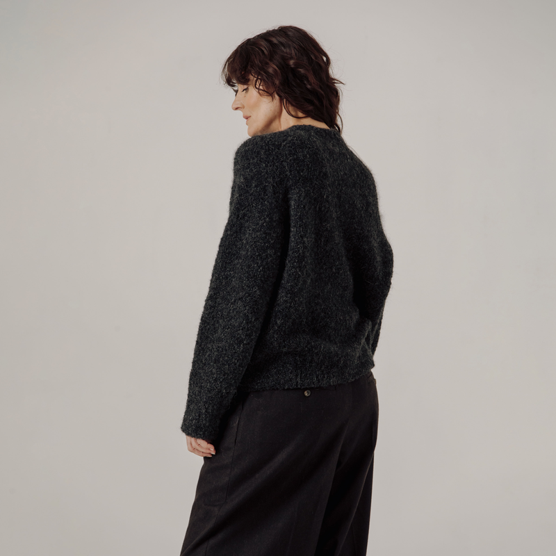 Person wearing a dark gray boucle sweater and black pants on a plain background