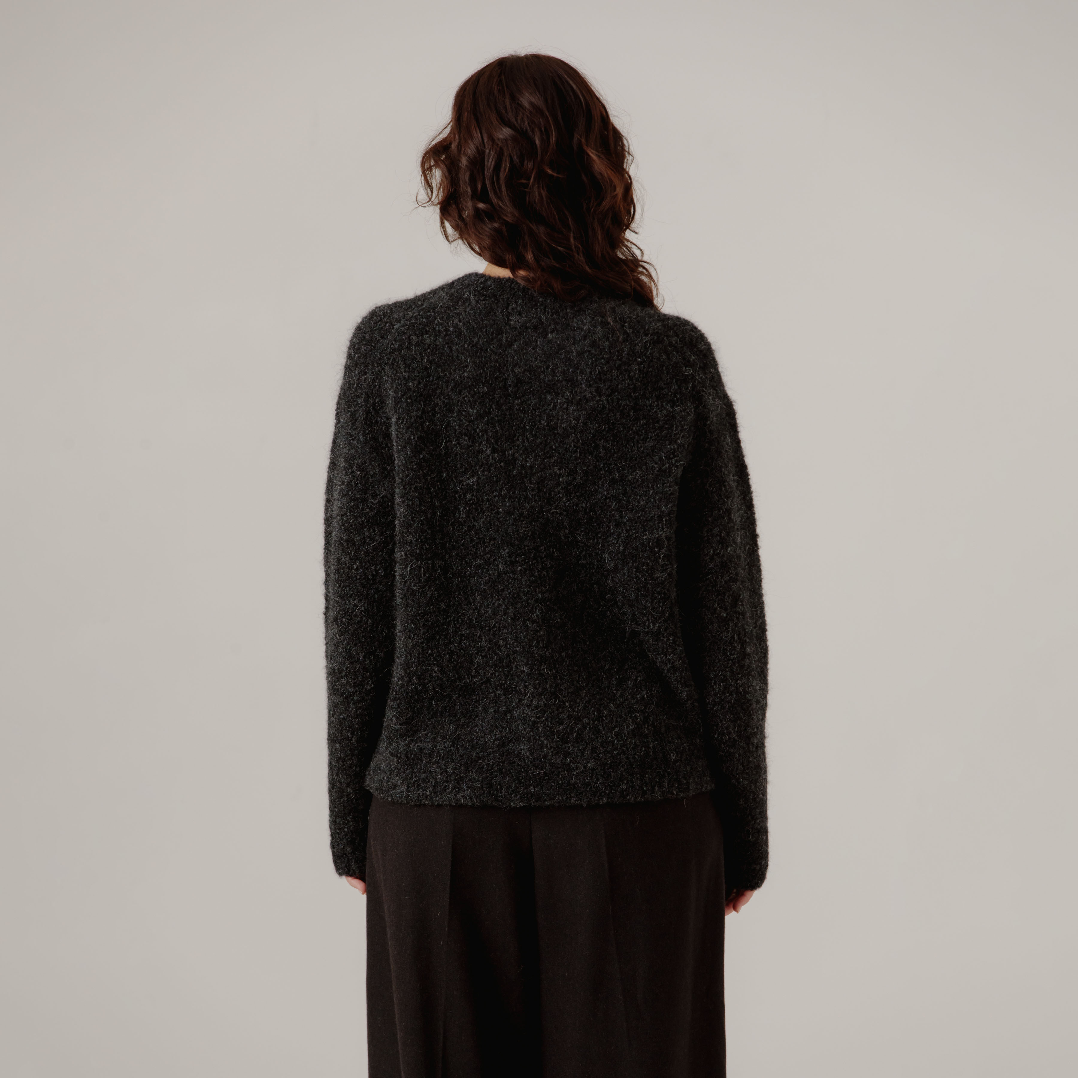 Person wearing a dark gray boucle sweater and black pants on a plain background