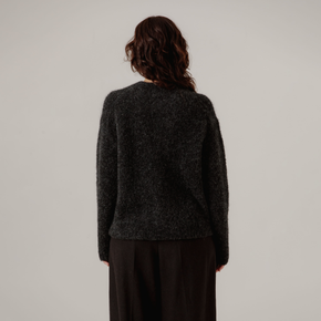 Person wearing a dark gray boucle sweater and black pants on a plain background