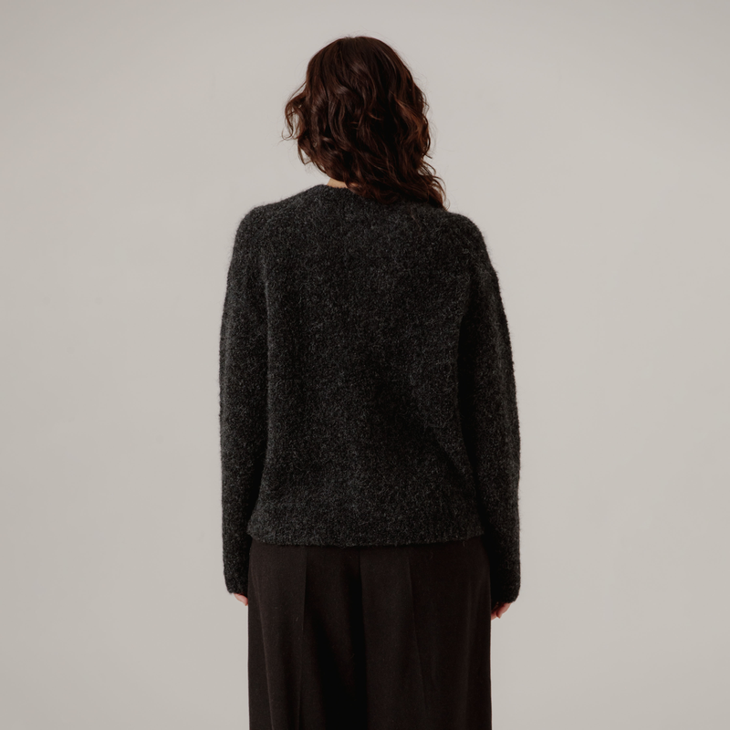 Person wearing a dark gray boucle sweater and black pants on a plain background