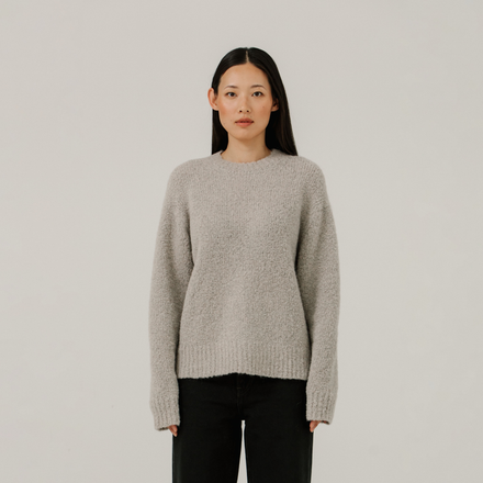 Woman wearing a light gray boucle sweater against a plain background