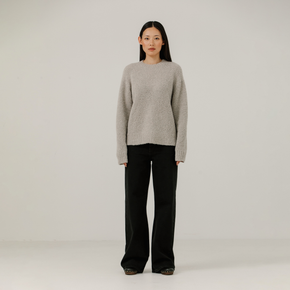 Woman wearing a light gray boucle sweater and black pants on a plain background