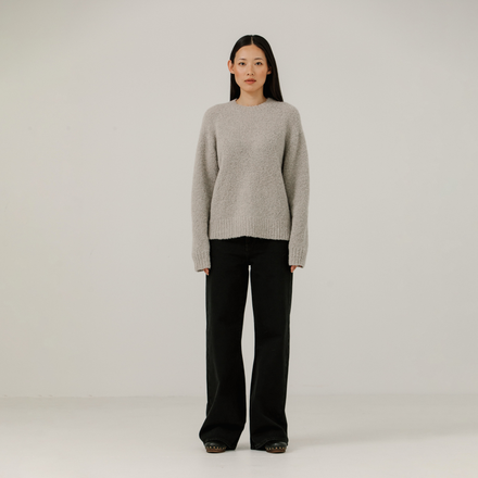 Woman wearing a light gray boucle sweater and black pants on a plain background