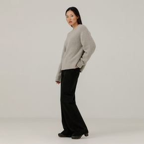 Woman wearing a light gray boucle sweater and black pants on a plain background
