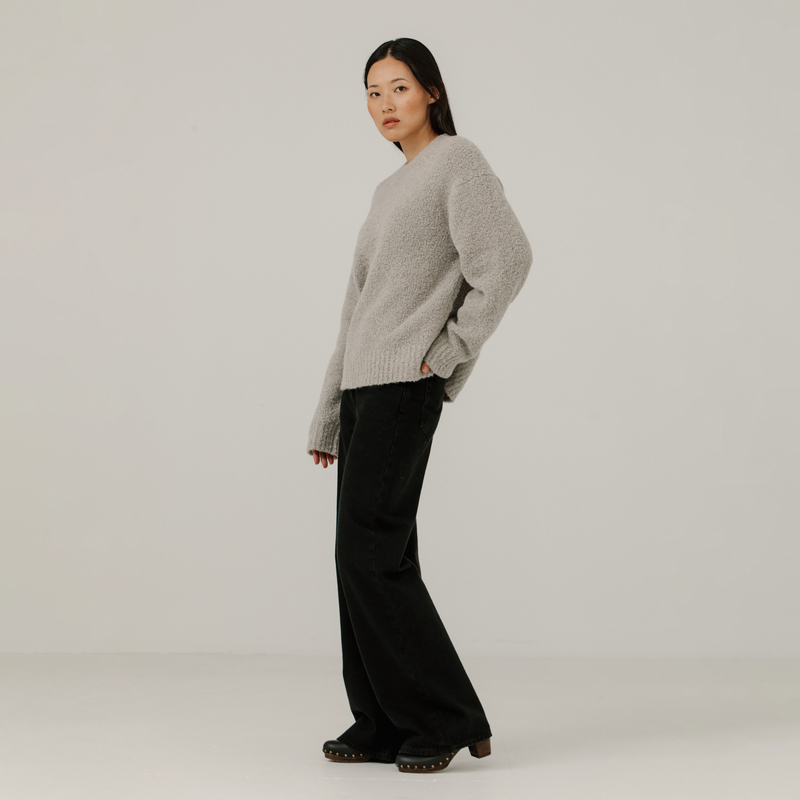 Woman wearing a light gray boucle sweater and black pants on a plain background