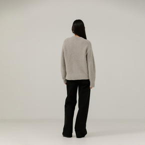 Person wearing a light grey boucle sweater and black pants on a plain background