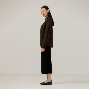 Woman wearing a brown sweater and black pants on a plain background