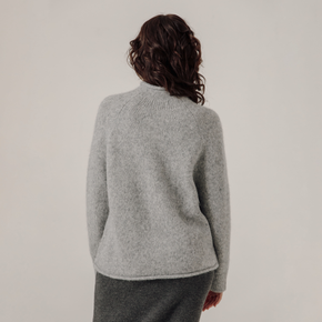 Person wearing a gray sweater and pants against a plain background