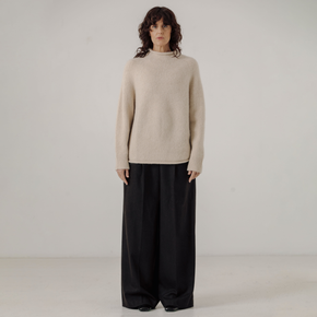 Woman wearing a white sweater and black pants against a plain background