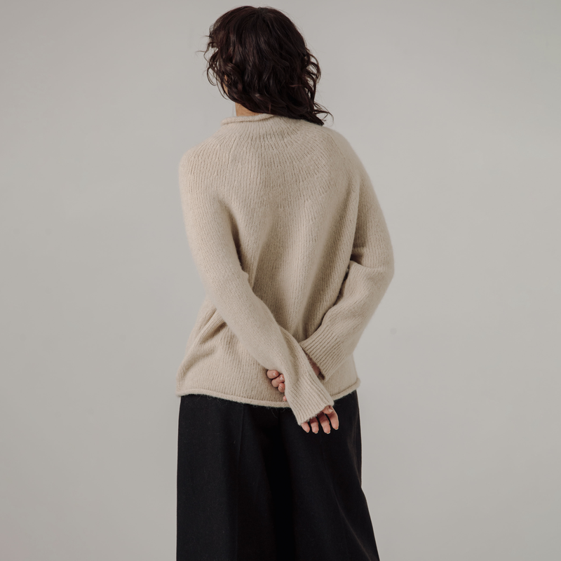 Person wearing a white sweater and black pants against a plain background