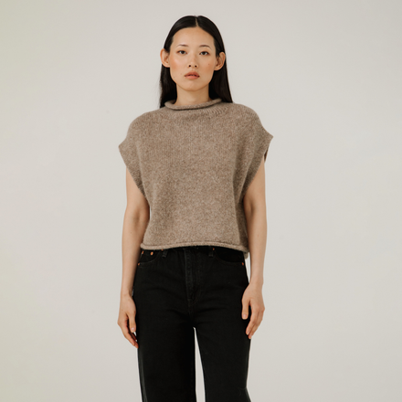 Woman wearing a beige knitted top and black pants against a plain background