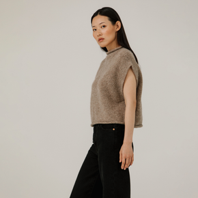 Woman wearing a beige sleeveless sweater against a plain background