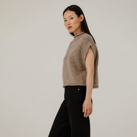 Woman wearing a beige sleeveless sweater against a plain background