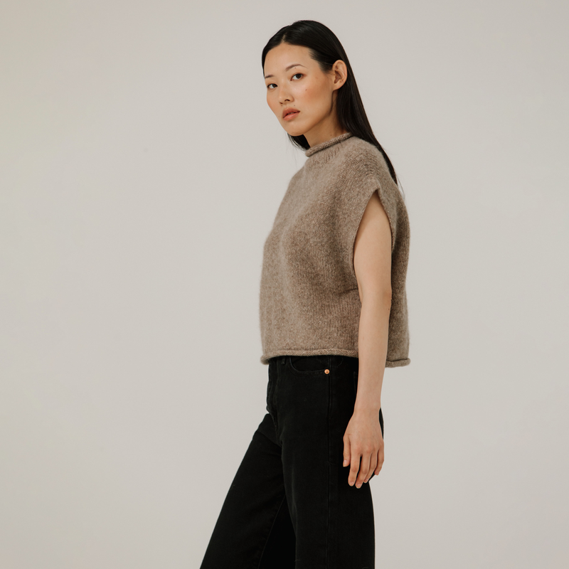 Woman wearing a beige sleeveless sweater against a plain background