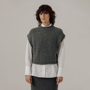 Woman wearing a gray knitted vest over a white shirt on a plain background