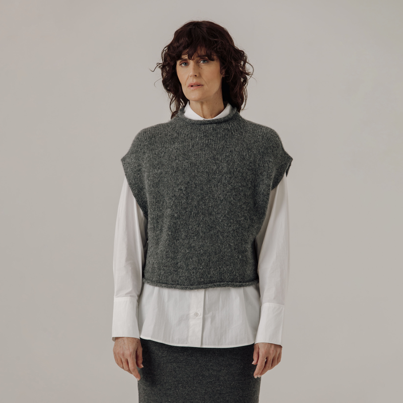 Woman wearing a gray knitted vest over a white shirt on a plain background