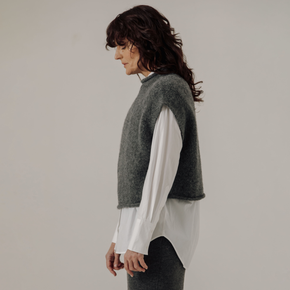 Woman wearing a gray sleeveless sweater over a white shirt against a plain background