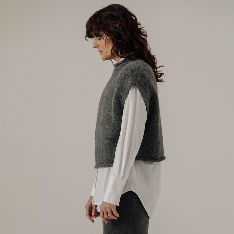 Woman wearing a gray sleeveless sweater over a white shirt against a plain background