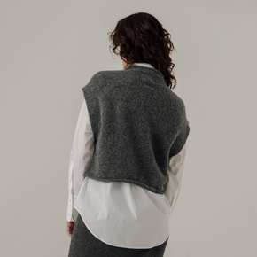 Person wearing a gray knitted vest over a white shirt on a plain background