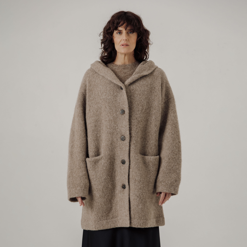 Woman wearing a beige hooded coat against a plain background