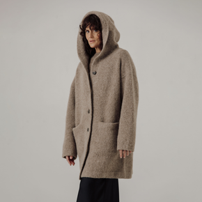 Person wearing a beige hooded coat on a plain background