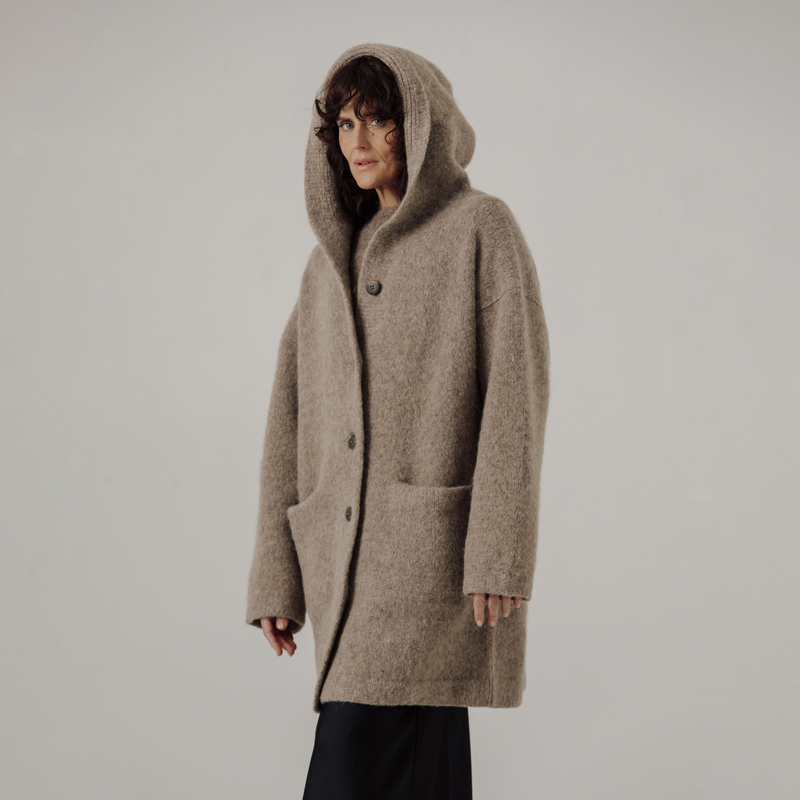 Person wearing a beige hooded coat on a plain background
