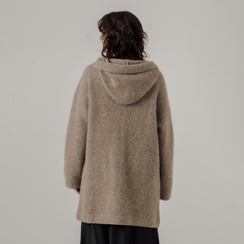 Person wearing a beige hooded coat against a plain background