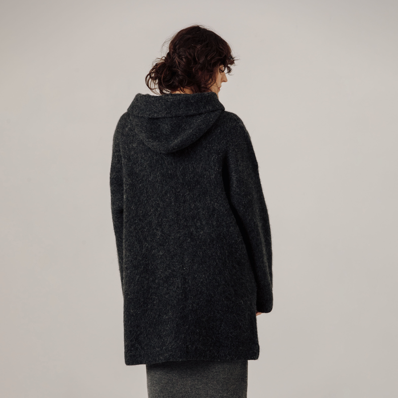Person wearing a dark gray hooded coat on a plain background