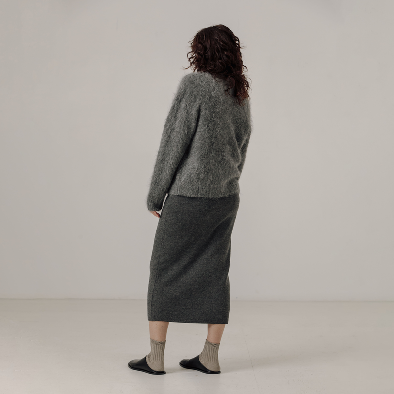 Person wearing a gray sweater and skirt set on a plain background