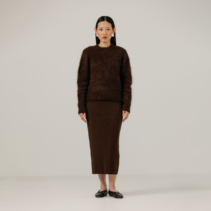 Woman wearing a brown textured sweater and skirt set on a plain background