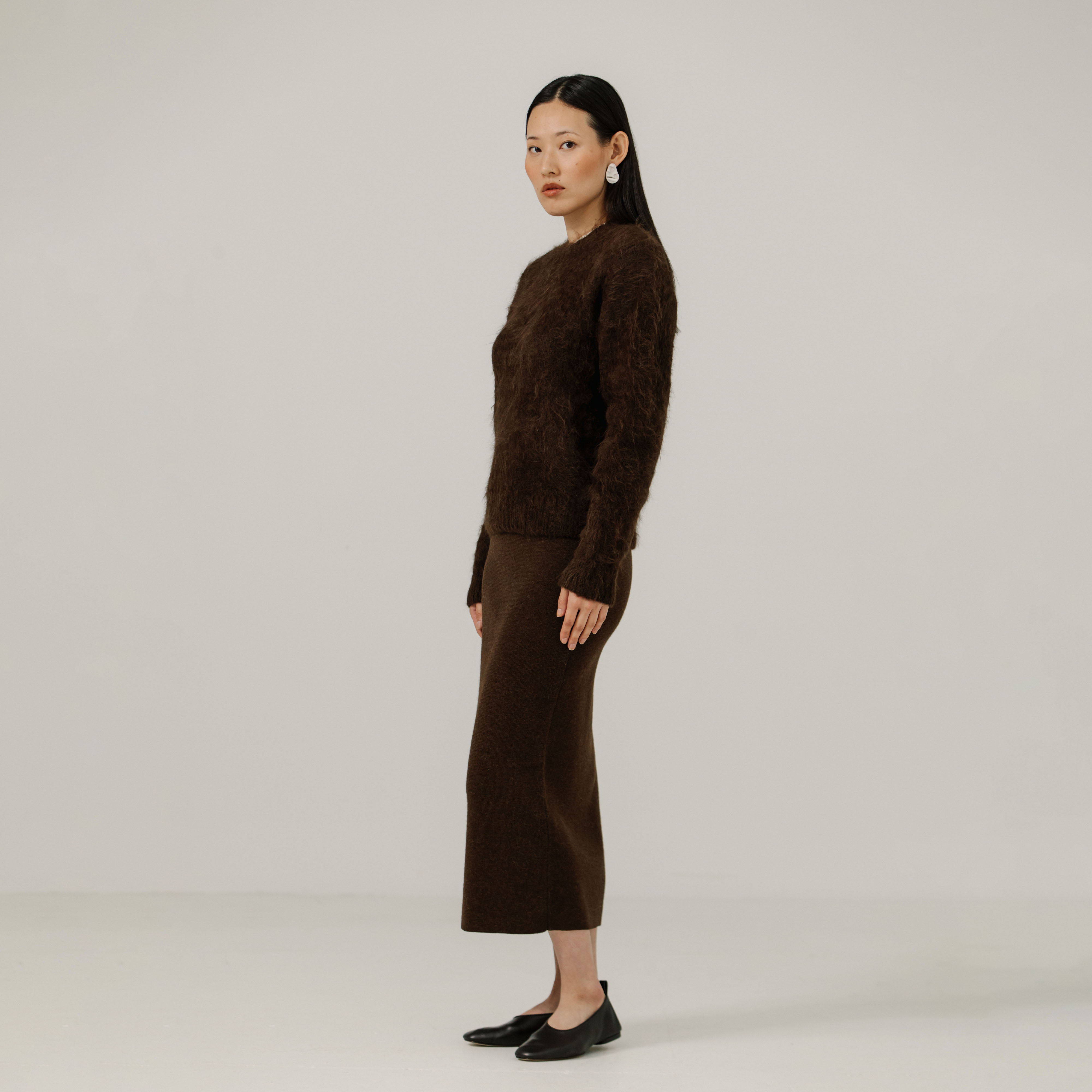 Woman wearing a brown textured sweater and brown skirt against a plain background