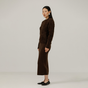 Woman wearing a brown textured sweater and brown skirt against a plain background
