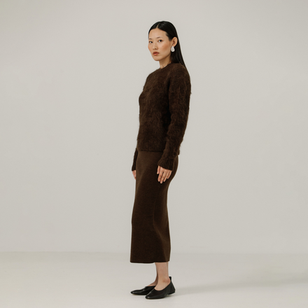 Woman wearing a brown textured sweater and brown skirt against a plain background