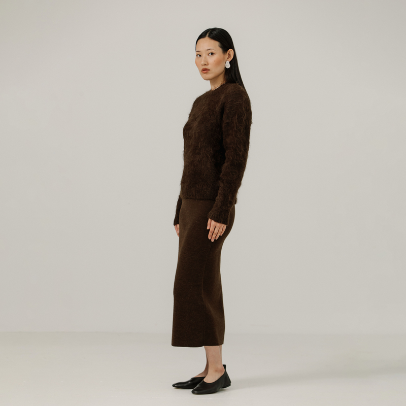 Woman wearing a brown textured sweater and brown skirt against a plain background