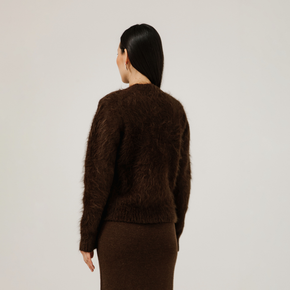 Person wearing a brown fuzzy sweater and skirt set on a plain background