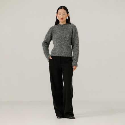 Woman wearing a gray textured sweater and black pants on a plain background