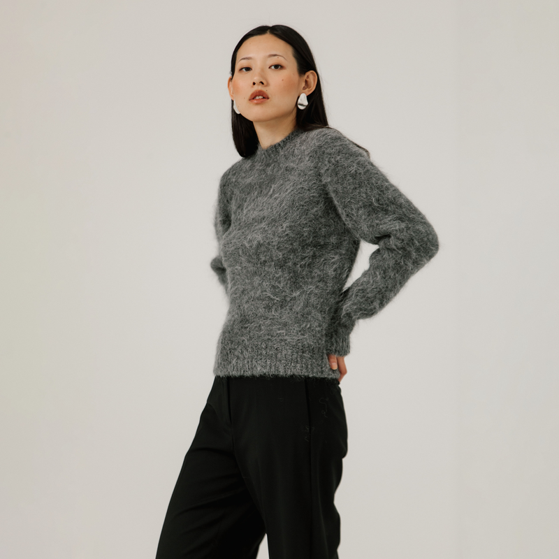 Woman wearing a gray textured sweater and black pants against a plain background