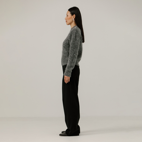 Woman wearing a gray textured sweater and black pants on a plain background
