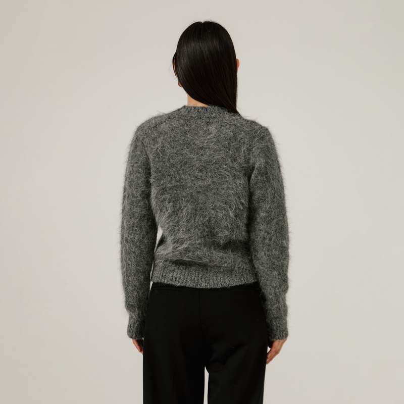 Person wearing a gray textured sweater and black pants against a plain background