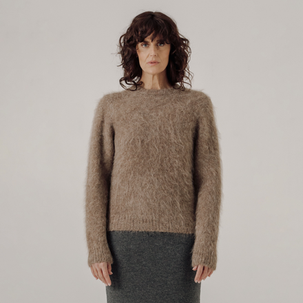 Woman wearing a light brown sweater against a plain background