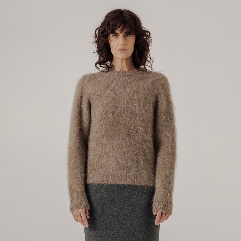 Woman wearing a light brown sweater against a plain background