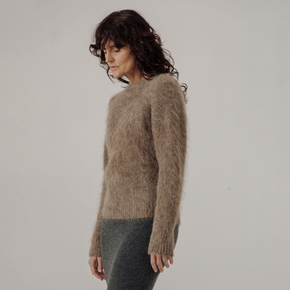 Woman wearing a light brown textured sweater against a plain background