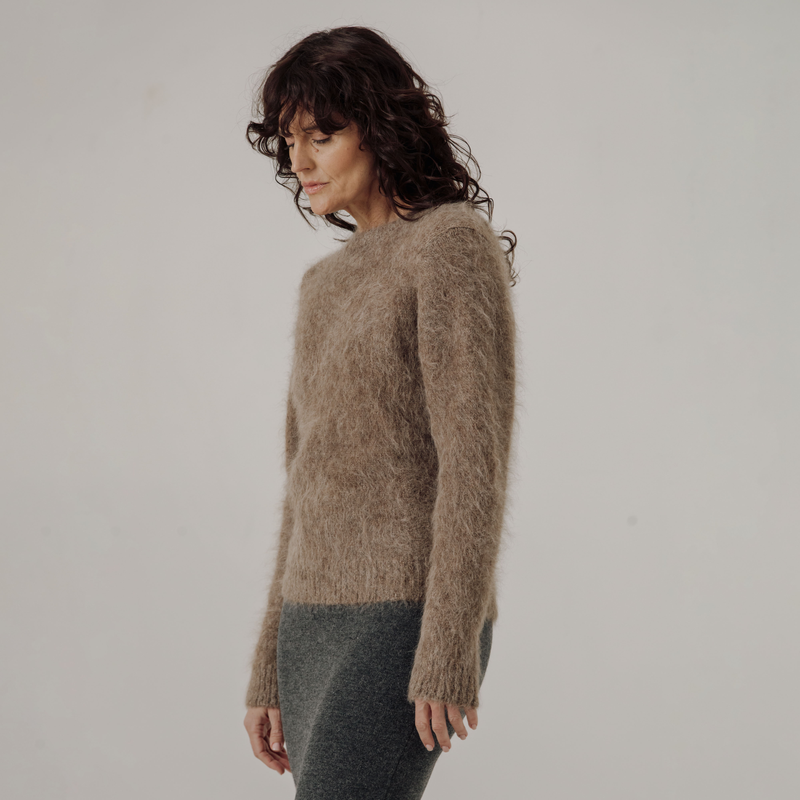 Woman wearing a light brown textured sweater against a plain background